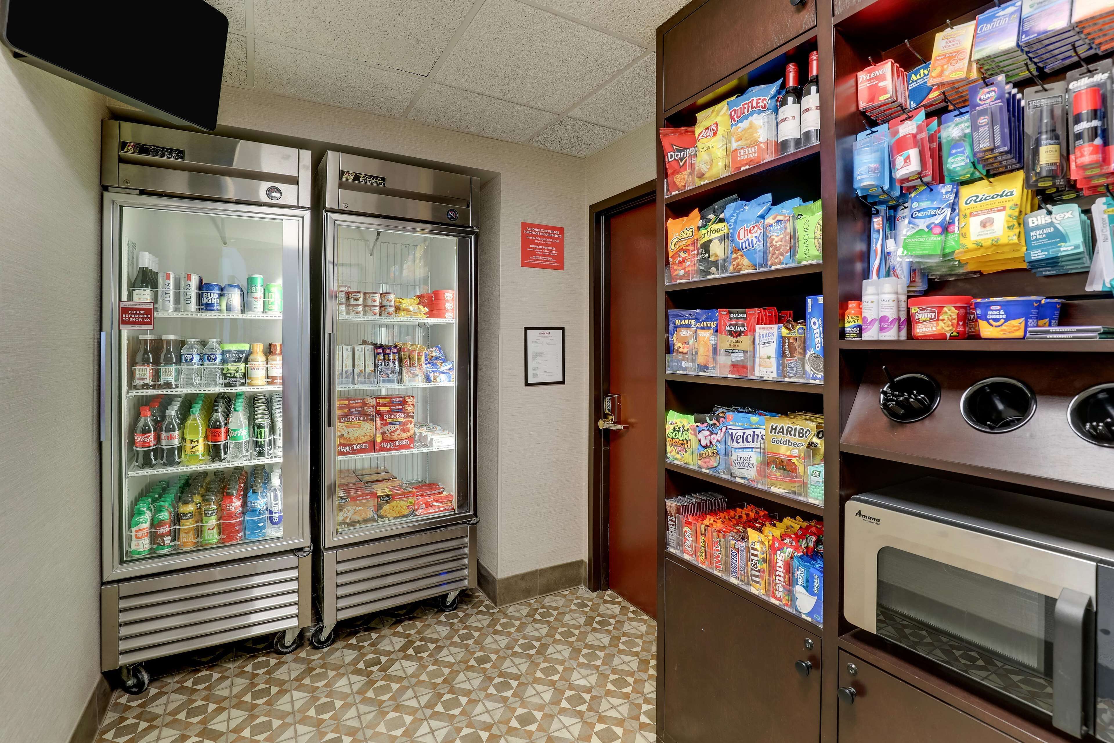 A kitchenette area with two refrigerators stocked with beverages and snacks, a microwave, and shelves with various food items.