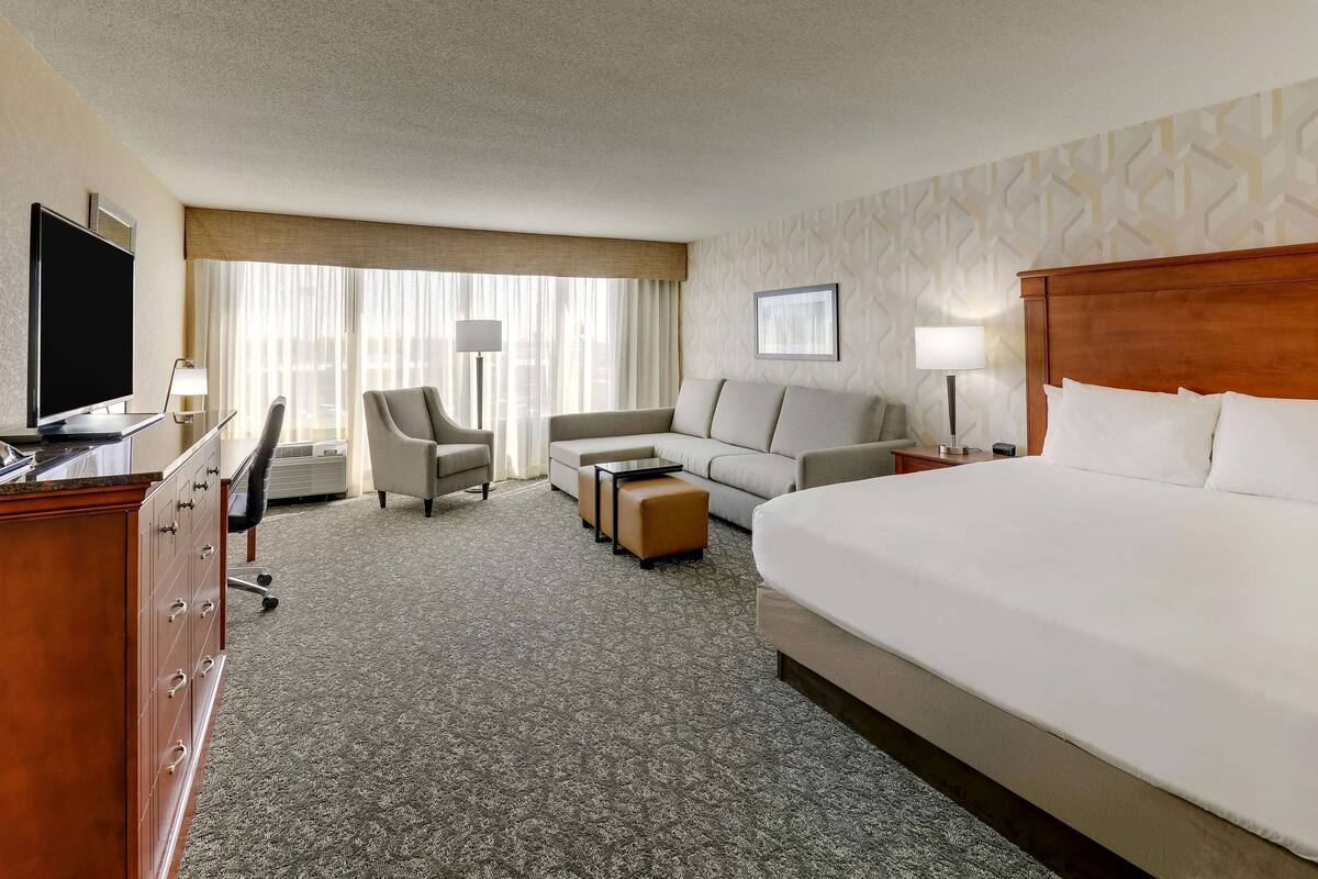 Quarto de hotel com uma cama grande, um sofá, uma escrivaninha com televisão e uma cadeira.