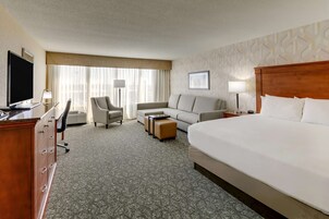Habitación de hotel con una cama grande, un sofá, un escritorio con televisor y una silla.