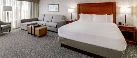 A hotel room with a large bed, a sofa, a chair, a small table, and two bedside tables with lamps.