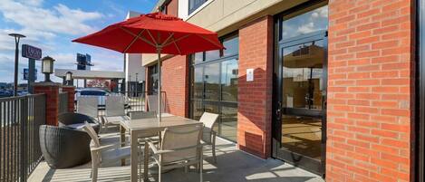An outdoor patio area with a table and chairs, a red umbrella, and a brick building facade.