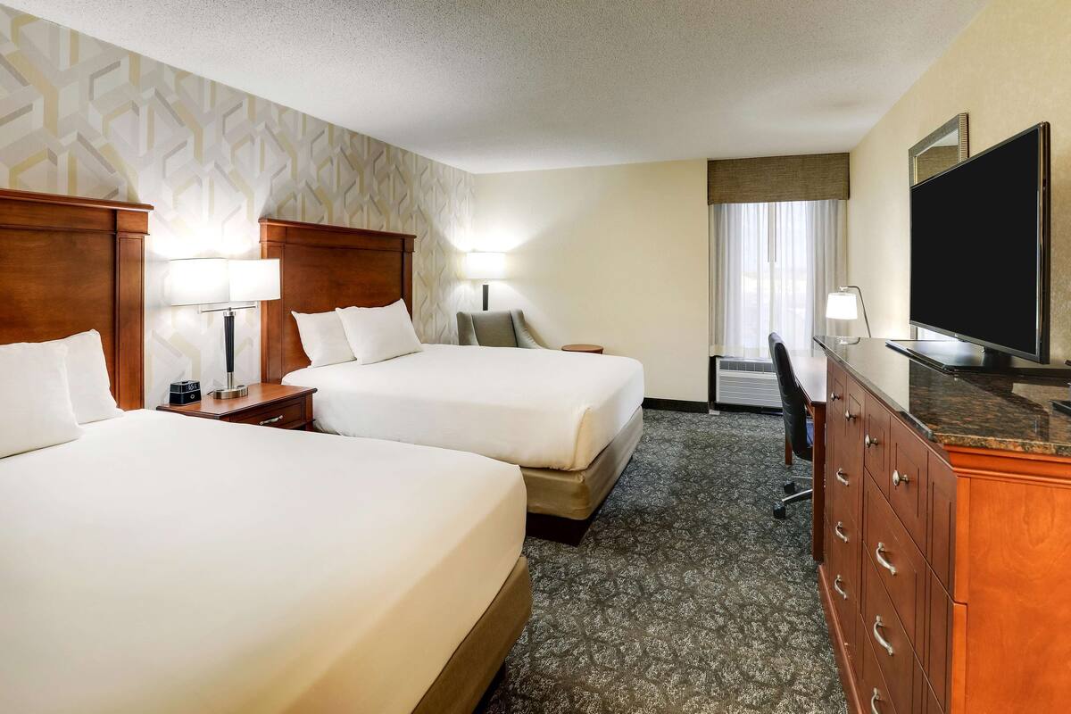 Quarto de hotel com duas camas, uma escrivaninha, uma televisão e um armário.