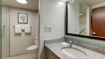 Une salle de bain dotée d’une douche à parois de verre, de toilettes, d’un lavabo avec un plan de travail en verre et d’une œuvre d’art encadrée accrochée au mur.