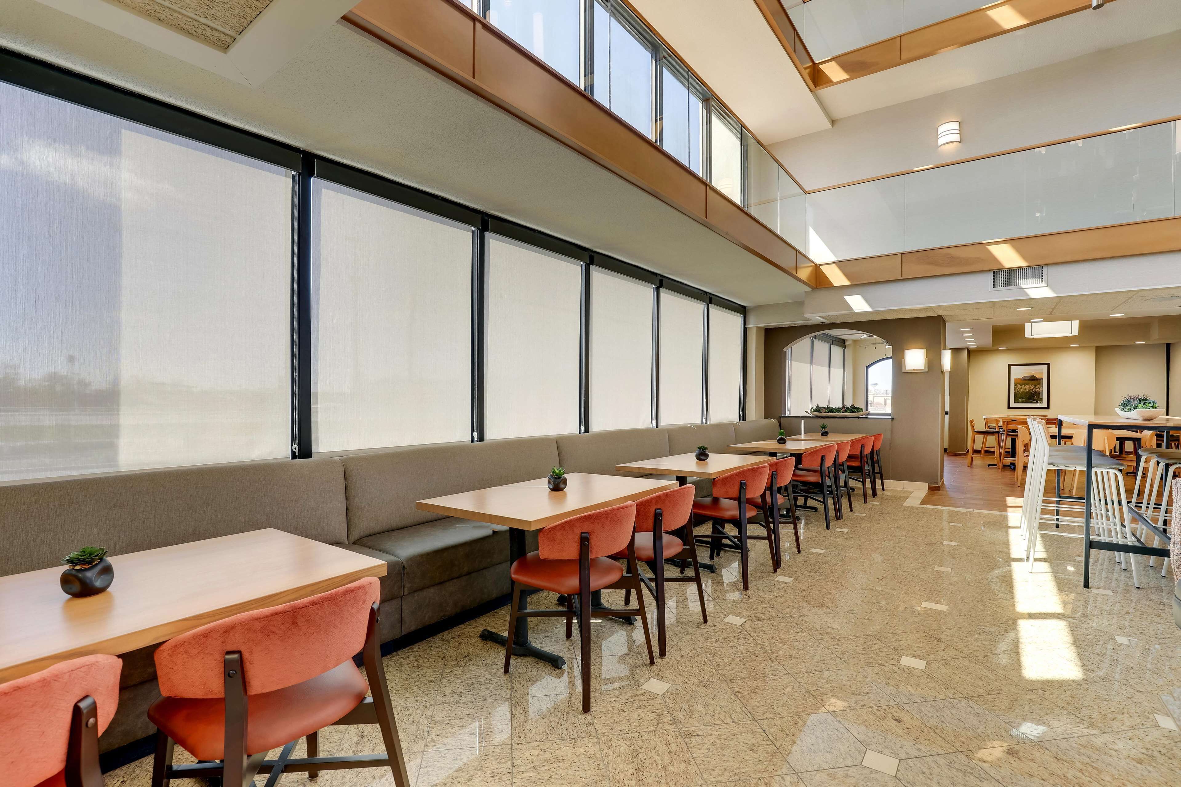 A modern dining area with multiple tables and chairs, large windows, and a high ceiling.