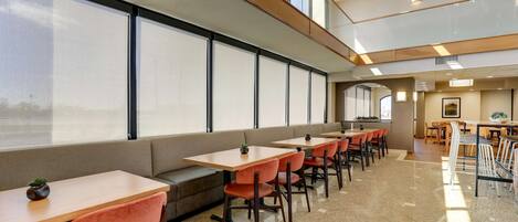 A modern dining area with multiple tables and chairs, large windows, and a high ceiling.