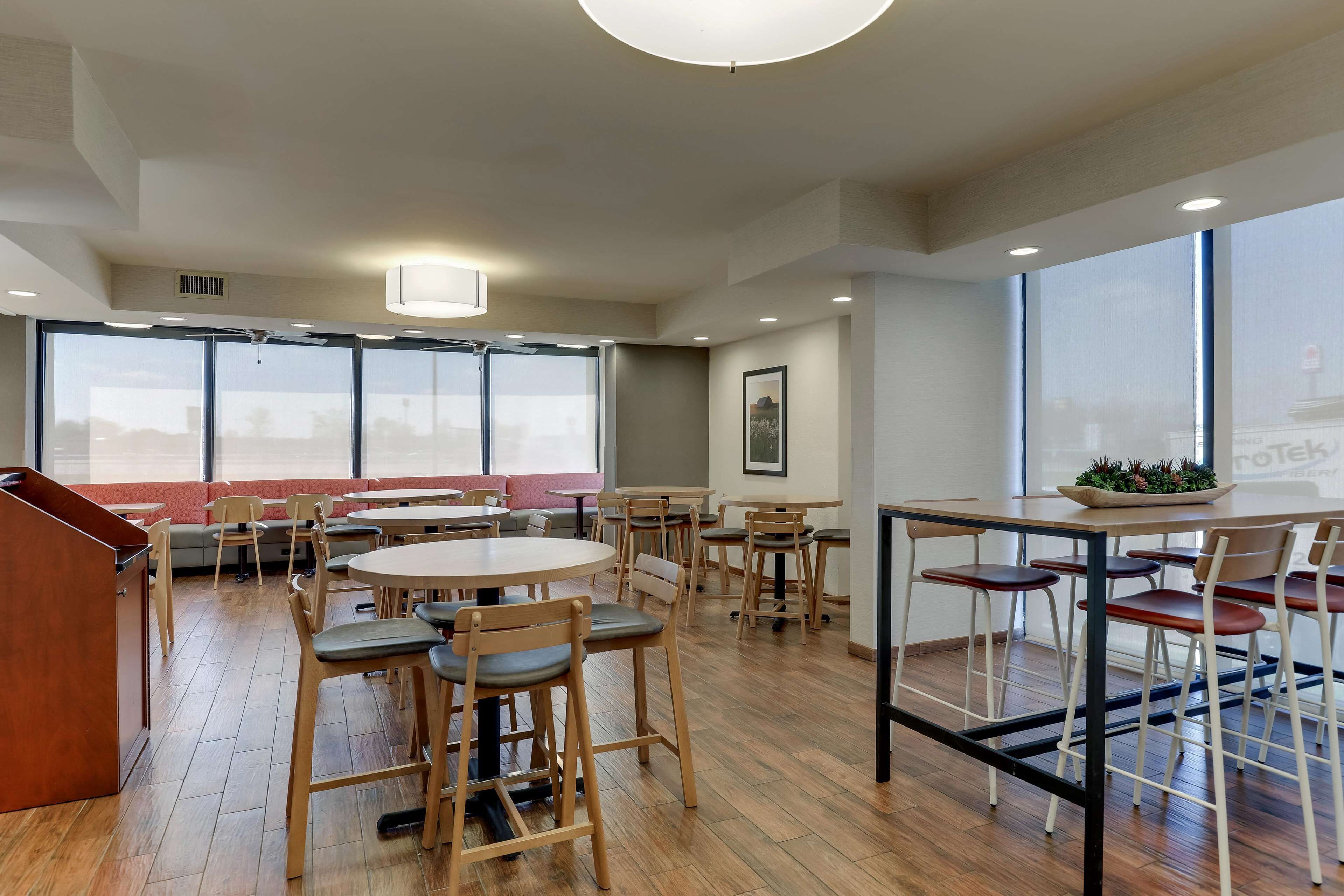 A modern dining area with round tables and chairs, large windows, and a central light fixture.