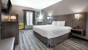 A hotel room with a large bed, a desk, a chair, a TV, and a nightstand with a lamp. - Best Western Heartland Inn (Mattoon)