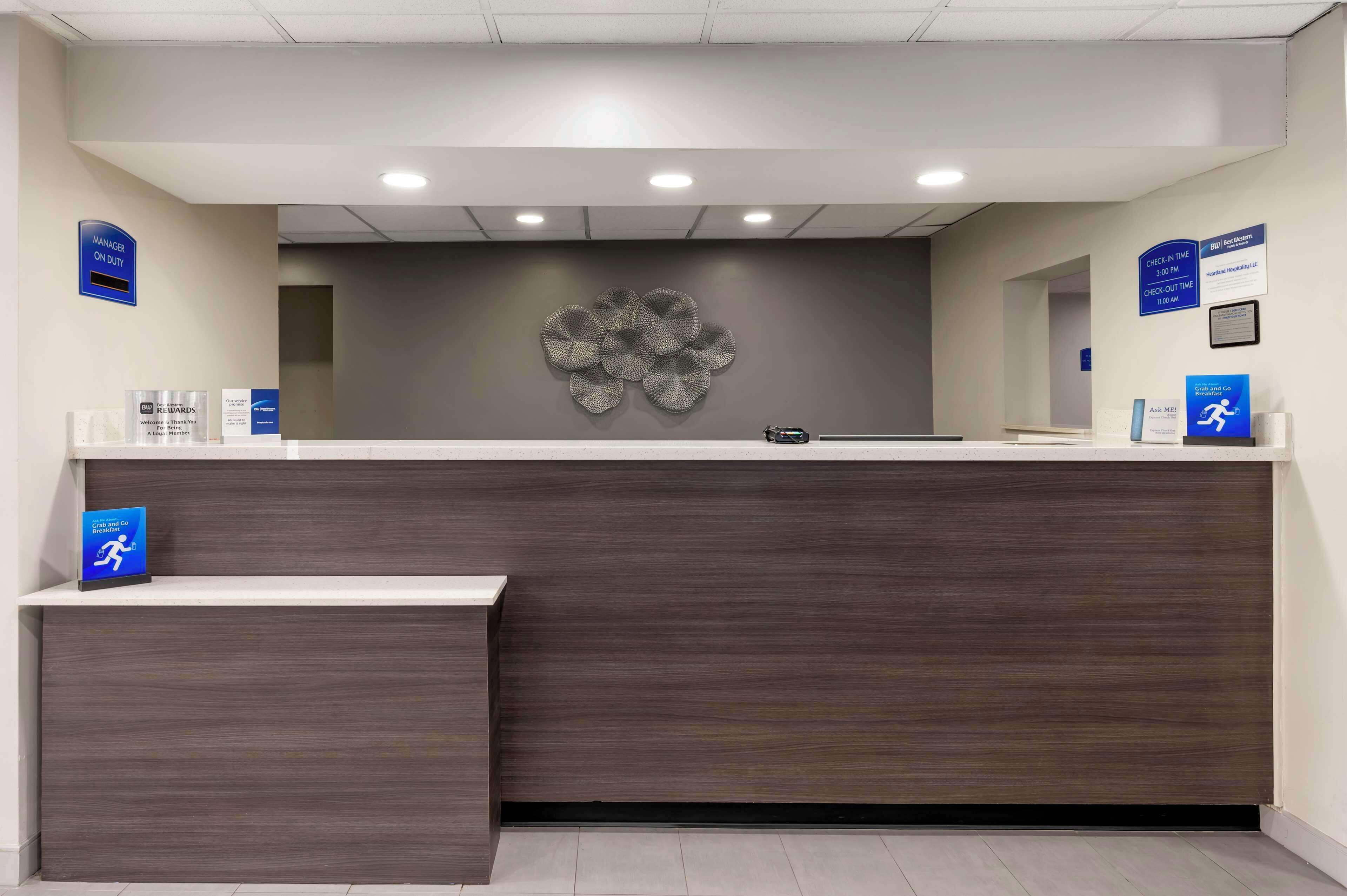 A reception desk with a dark wood finish, a wall-mounted flower decoration, and signs indicating check-in and check-out times.