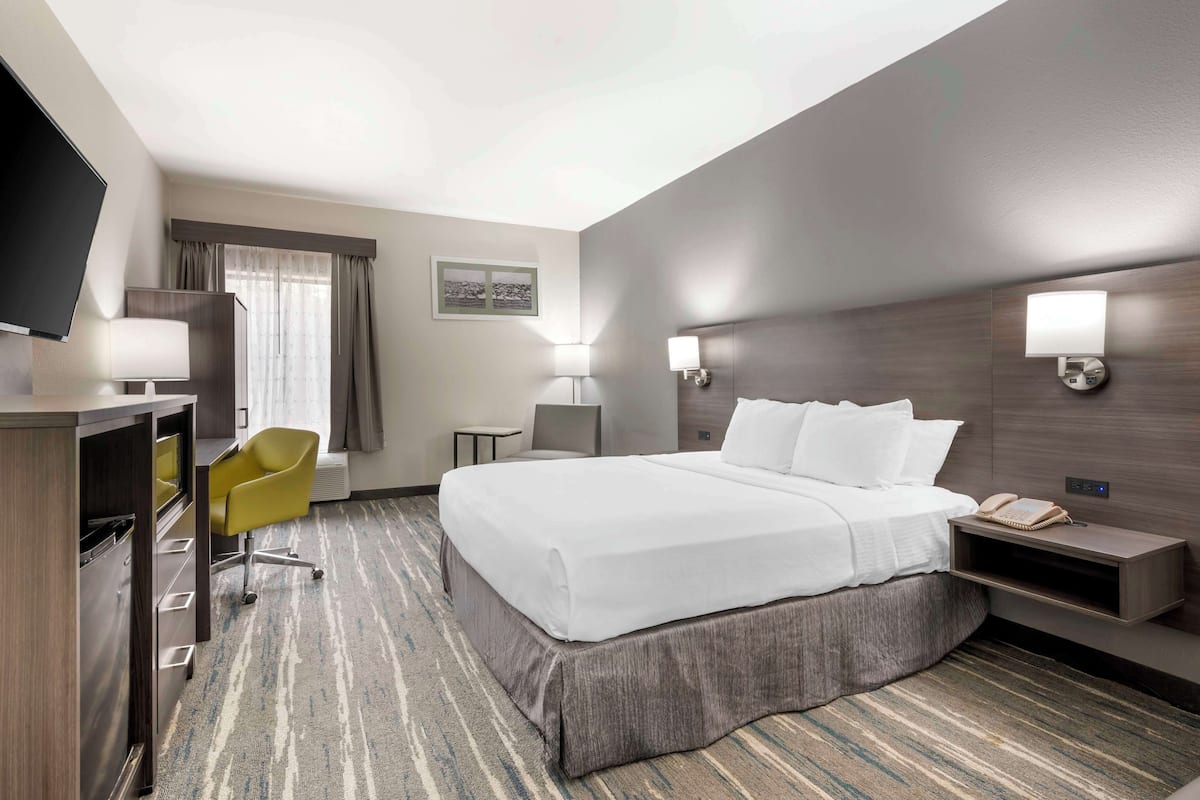 A hotel room with a large bed, a desk with a chair, a flat-screen TV, and a wall-mounted lamp.