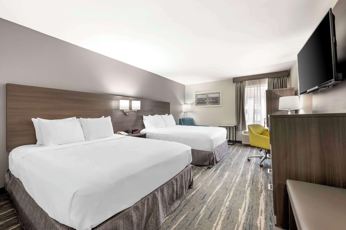 A hotel room with two beds, a desk, a chair, a TV, and a window with curtains.