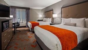 A hotel room with two beds, a desk with a chair, a TV, and a minibar.
