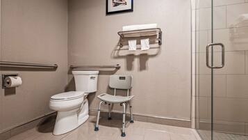 A bathroom with a toilet, a handrail, a grab bar, a shower area, and a towel rack.