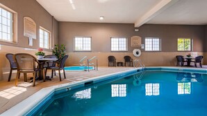An indoor swimming pool with clear water, surrounded by lounge chairs and tables.