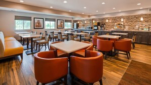 A restaurant with multiple tables and chairs, a kitchen area, and framed pictures on the wall.