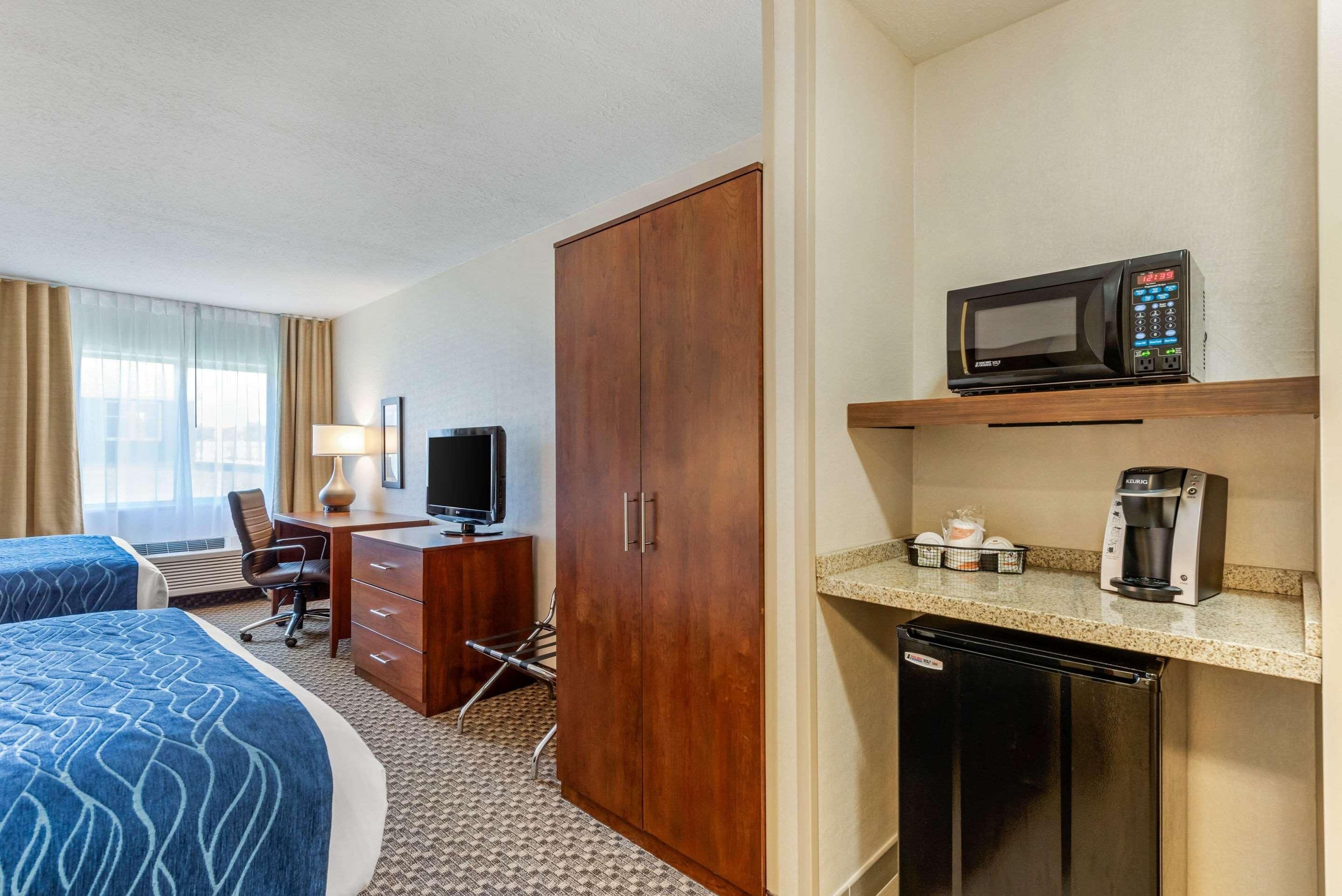 A hotel room with a bed, desk, chair, television, wardrobe, microwave, coffee maker, and refrigerator.