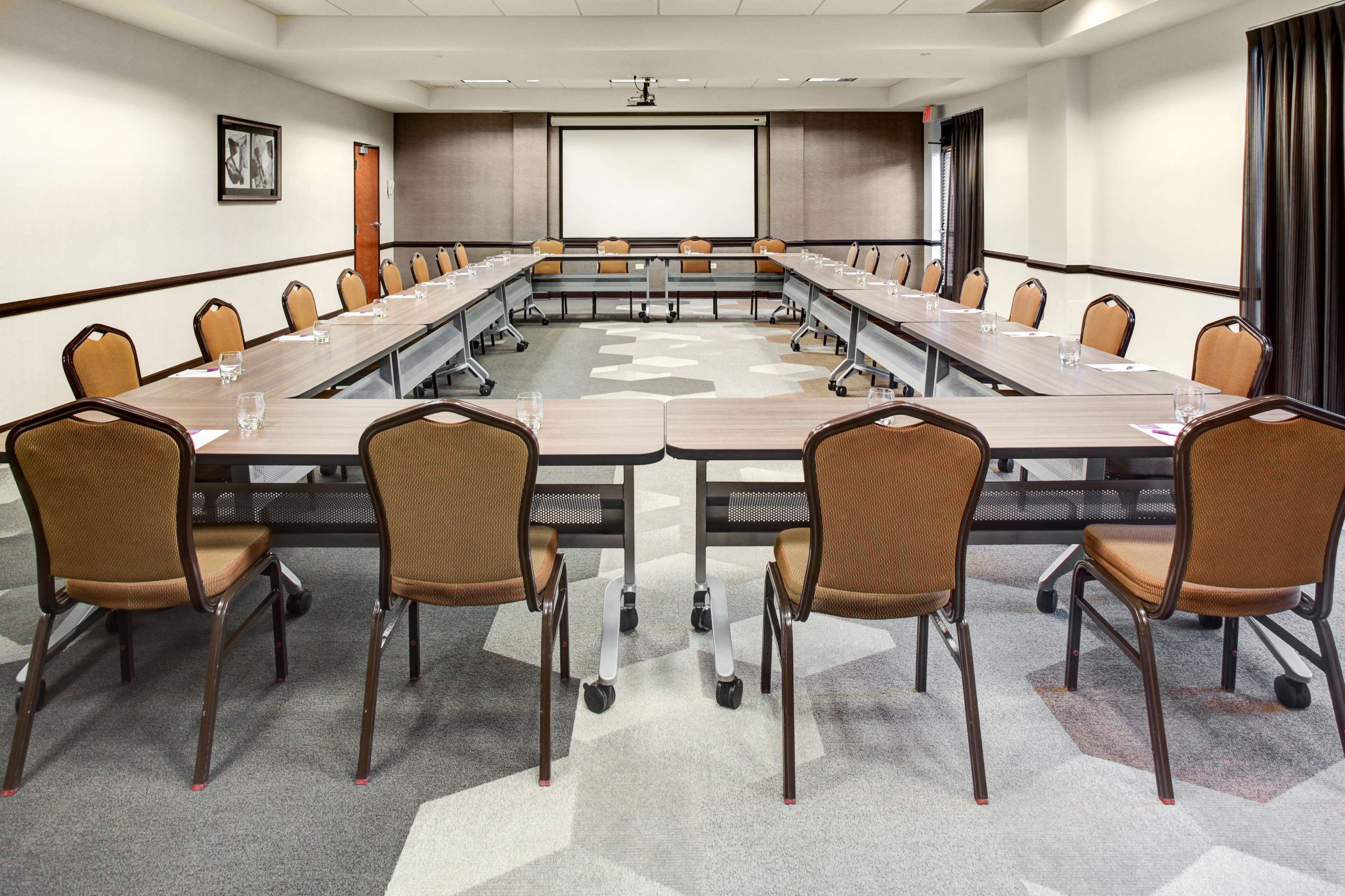 A conference room with a long table, chairs, a projector screen, and a carpeted floor.