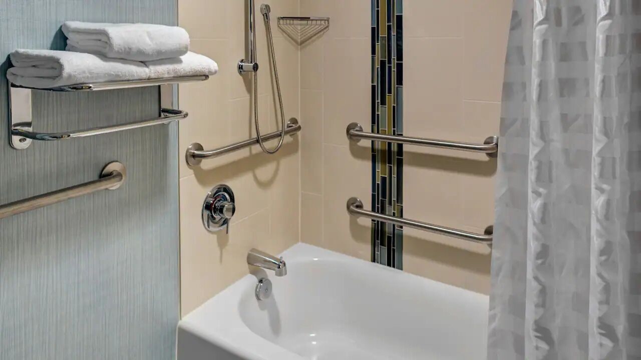 Baño con bañera, barras de apoyo, toallero y cabezal de ducha.