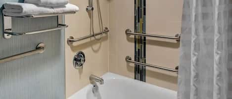 A bathroom with a bathtub, handrails, a towel rack, and a shower head.