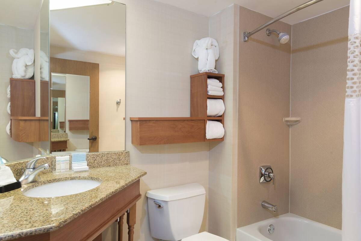 Een badkamer met een wastafel, toilet en douche. Er staan houten planken met handdoeken.
