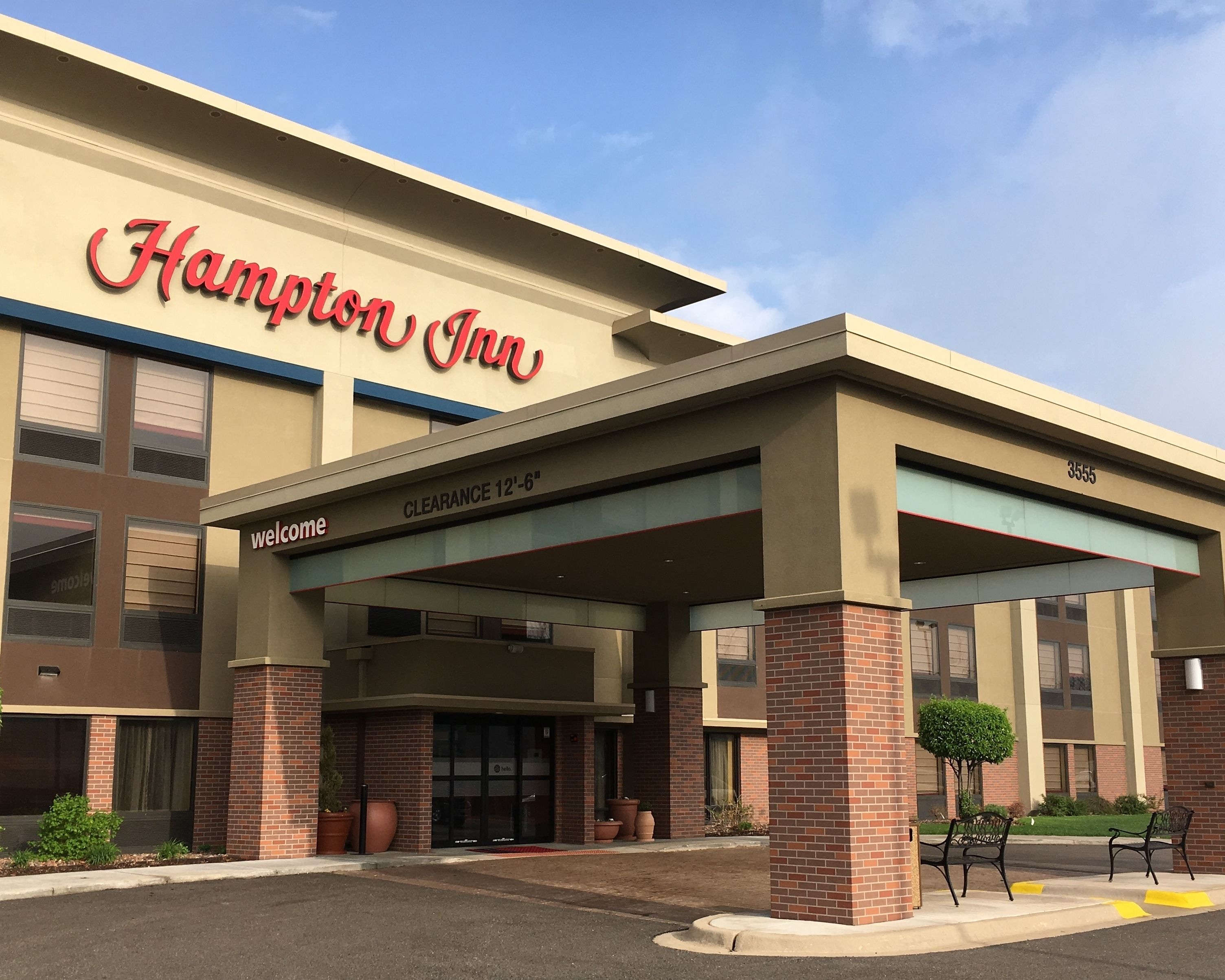 A Hampton Inn hotel entrance with a clear sign, a covered entrance, and a parking area.