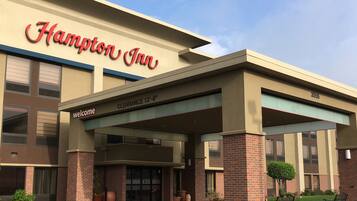A Hampton Inn hotel entrance with a clear sign, a covered entrance, and a parking area.