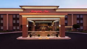 Entrada d'un hotel Hampton Inn amb façana de maó, finestres grans i una zona d'entrada ben il·luminada.