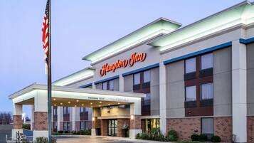 Een Hampton Inn hotel met een heldere ingang, een vlaggenmast en een bord dat een hoogte van 3,6 meter aangeeft.