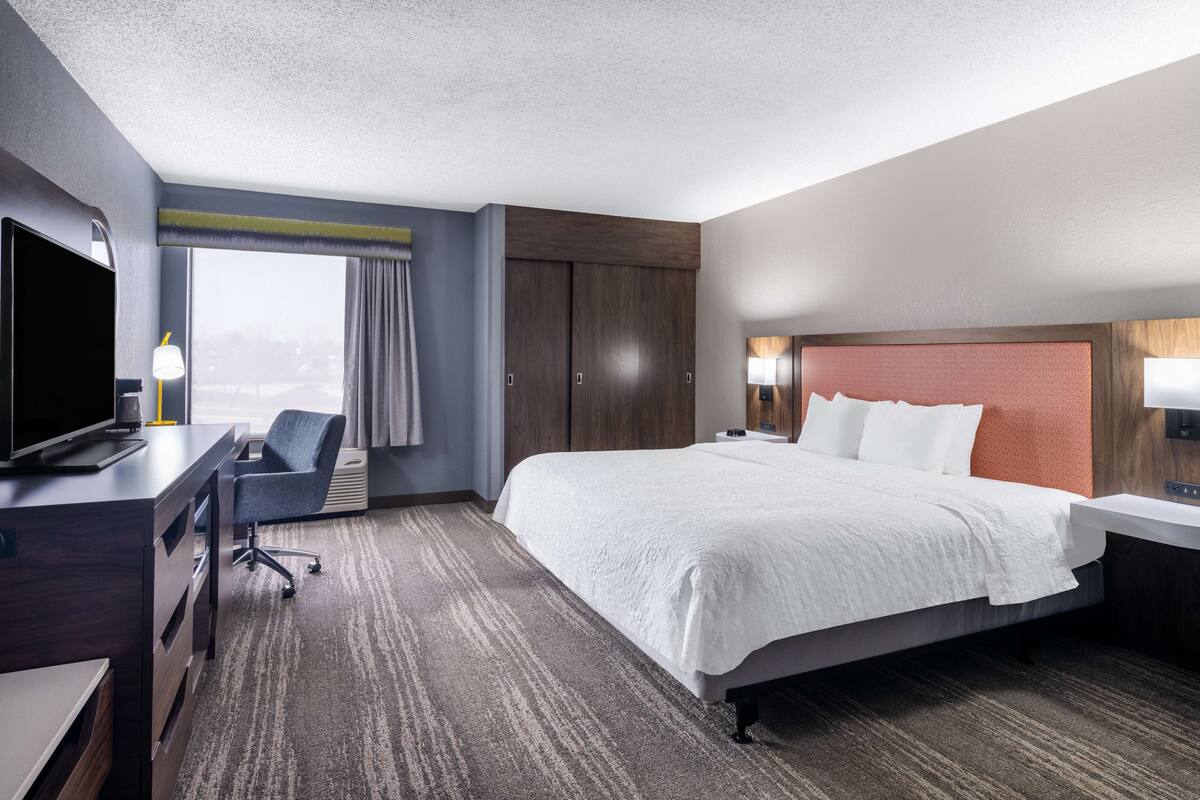 Een hotelkamer met een groot bed, een bureau met een computer, een stoel en uitzicht op het landschap.