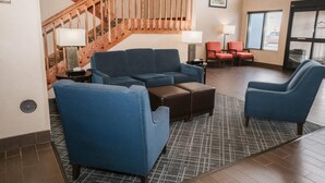 A spacious lobby with a blue sofa set, a wooden staircase, and a large window.