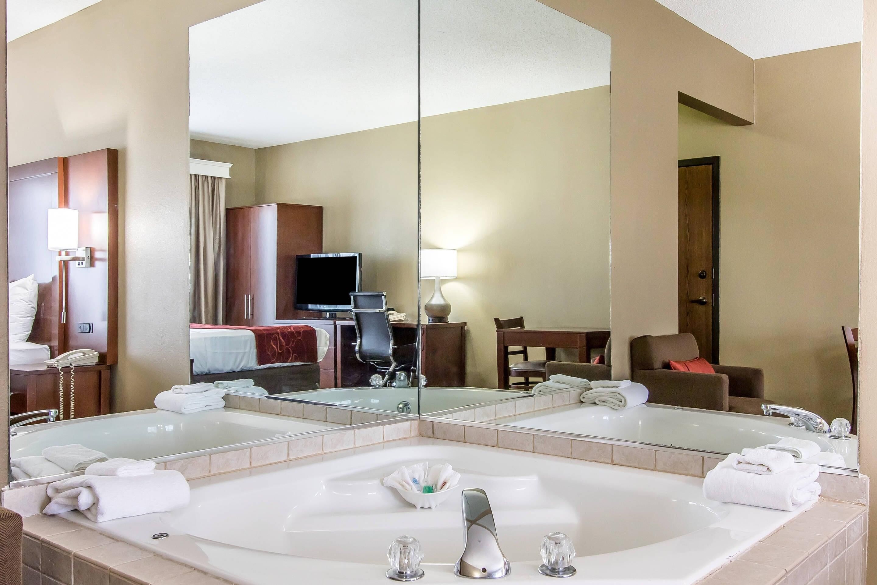 Ein Hotelbad mit einem großen Spiegel, einer Badewanne und einer Sitzecke mit Schreibtisch und Stühlen.