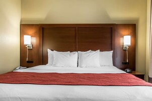 Una habitación de hotel con una cama grande, dos lámparas de noche, un teléfono y una manta roja.