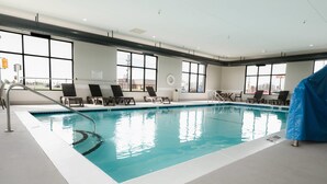 An indoor swimming pool with clear water, sun loungers, and large windows.