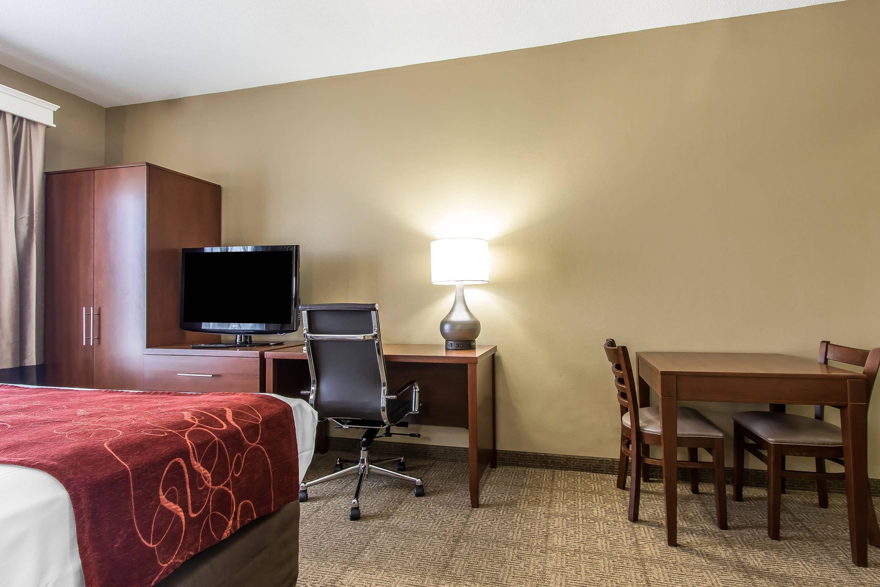 Una habitación de hotel con cama, escritorio, silla, televisor y lámpara.