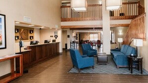 A hotel lobby with a reception desk, blue seating area, a staircase, and a dining area.