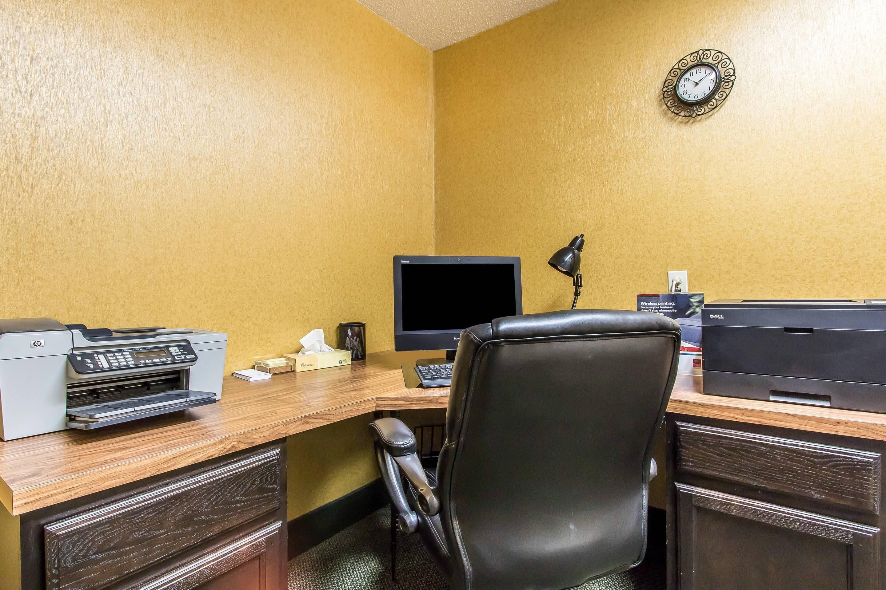 Un bureau d’hôtel équipé d’un bureau, d’un ordinateur, d’une imprimante et d’une chaise.