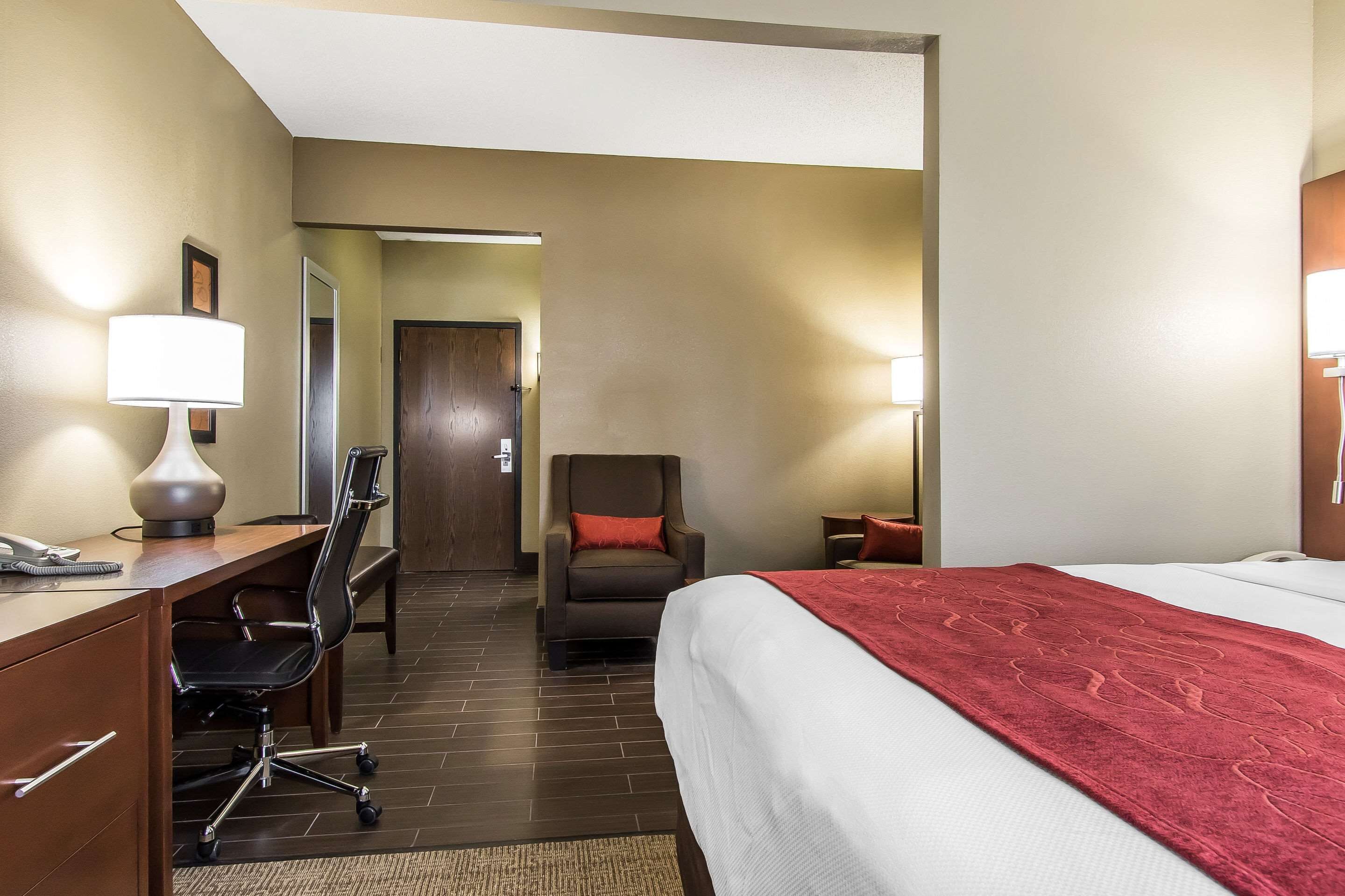 A hotel room with a bed, desk, chair, and a door leading to another room.