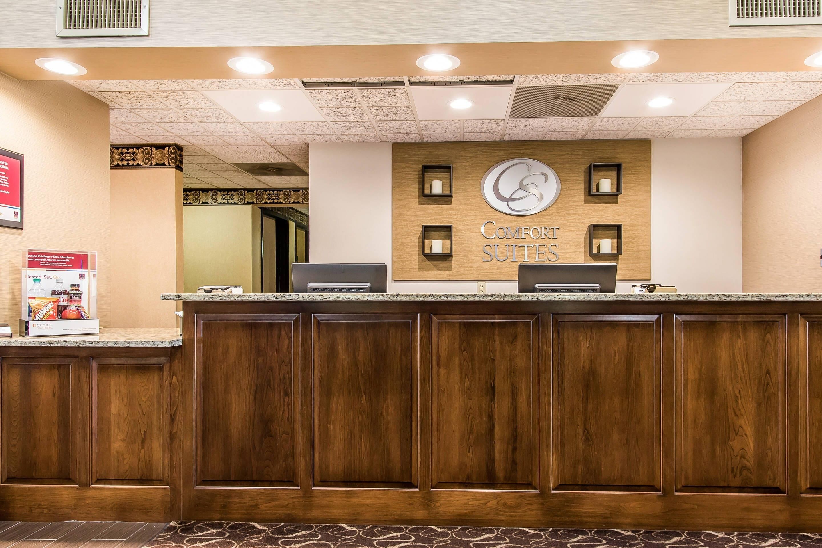 A reception desk with a wooden panel design, a sign reading 'Comfort Suites,' and a counter with a computer and a small display.