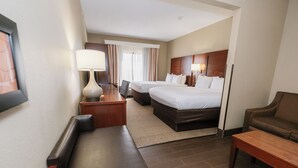 A hotel room with two beds, a desk, a chair, a sofa, and a lamp.