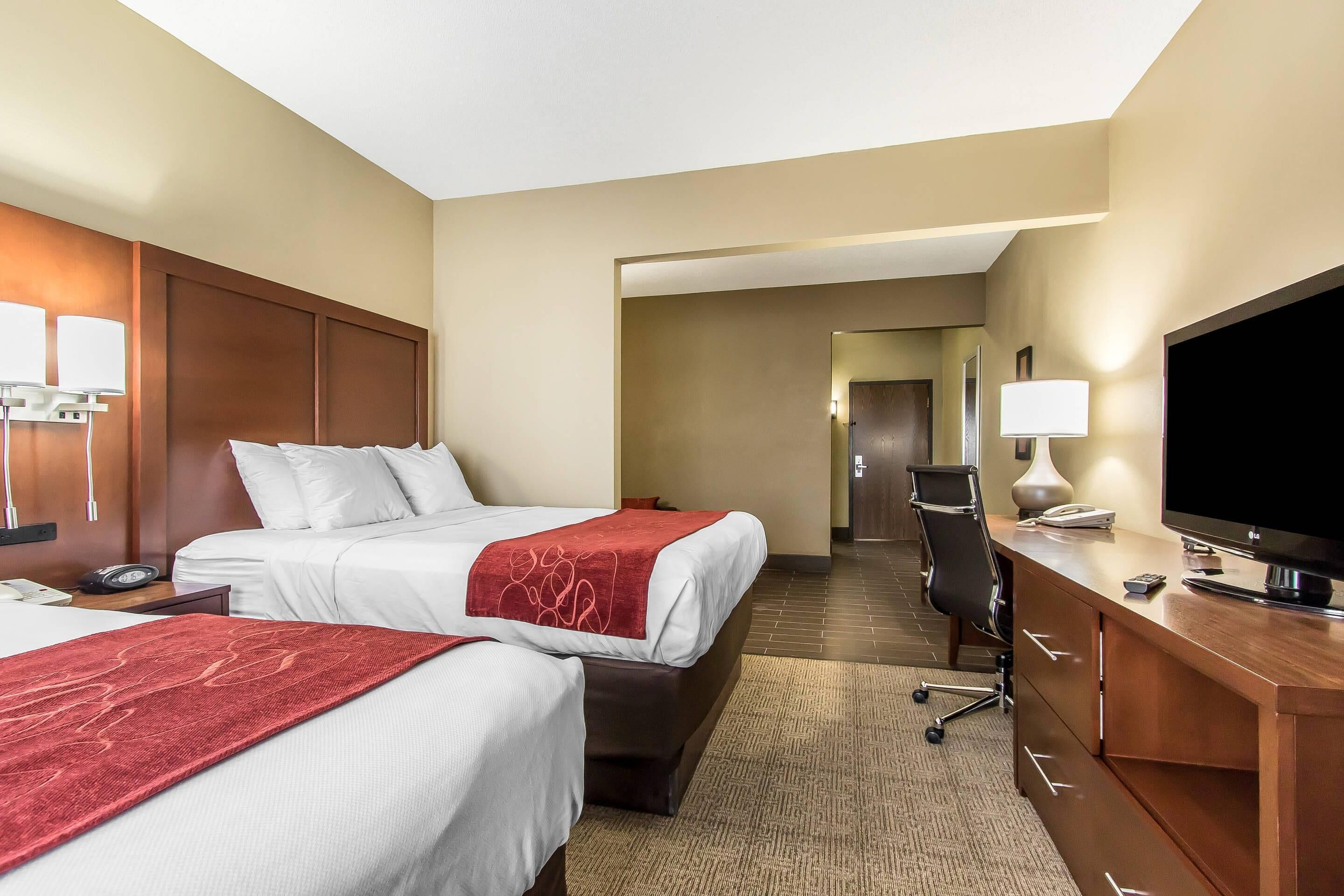 Ein Hotelzimmer mit zwei Betten, einem Schreibtisch mit Fernseher und einem Spiegel.