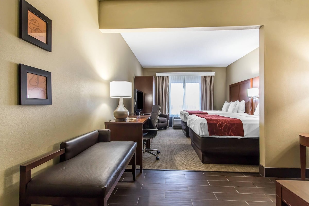 A hotel room with a bed, a desk with a chair, a sofa, a TV, and framed pictures on the wall.