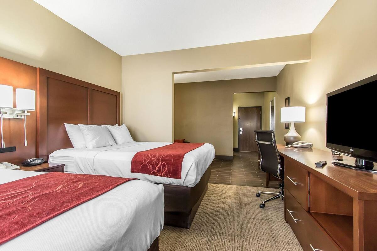 A hotel room with two beds, a desk with a TV, and a separate area with a chair and desk.