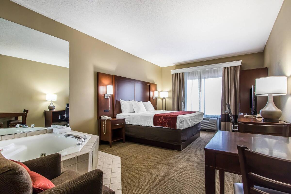 A hotel room with a large bed, a separate bathroom with a bathtub, a desk, and a chair.
