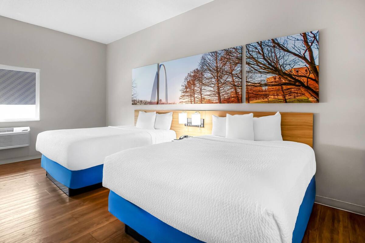 A hotel room with two beds, a large window, and a wall-mounted artwork.