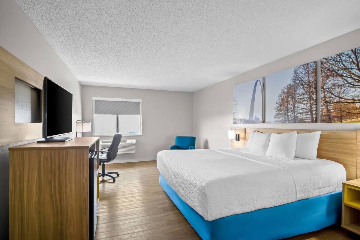 A modern hotel room with a large bed, a desk with a computer, a chair, and a TV.