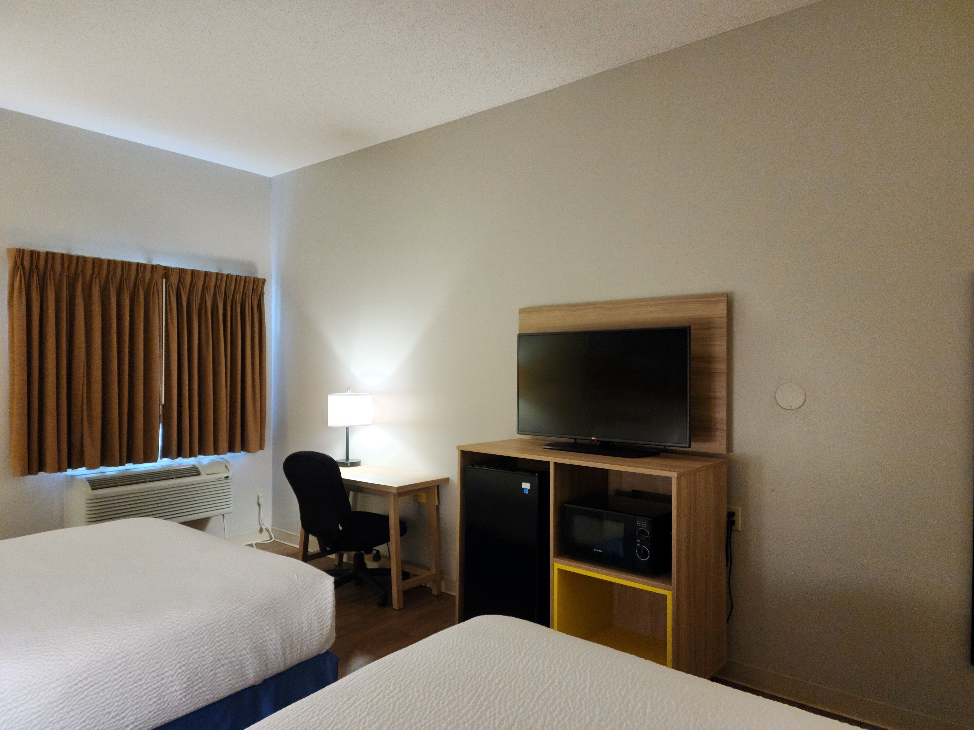 A hotel room with two beds, a desk with a lamp, a television, and a microwave.
