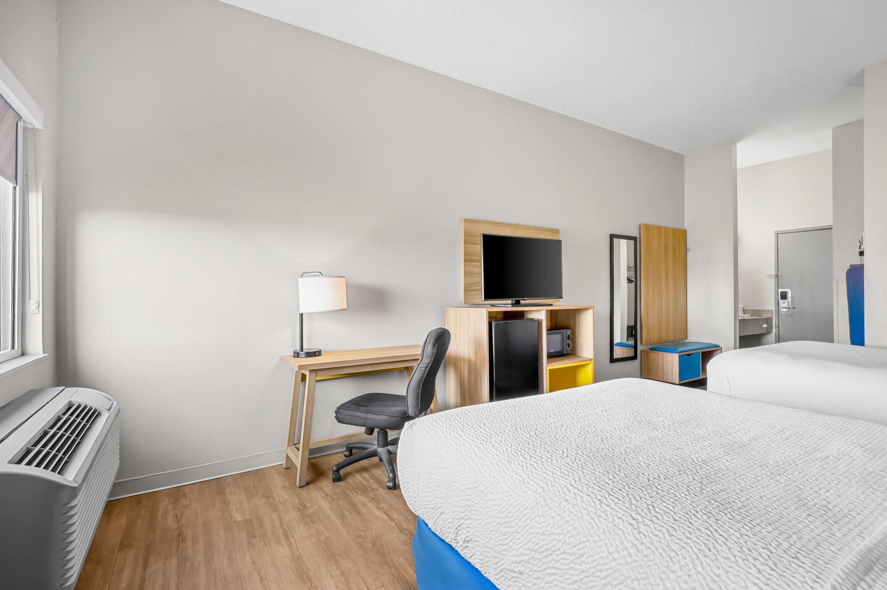A hotel room with a bed, desk, chair, TV, and a small kitchenette.