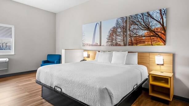A modern hotel room with a large bed, a blue chair, and a wall-mounted TV. - Days Inn by Wyndham Collinsville/St. Louis (Collinsville)