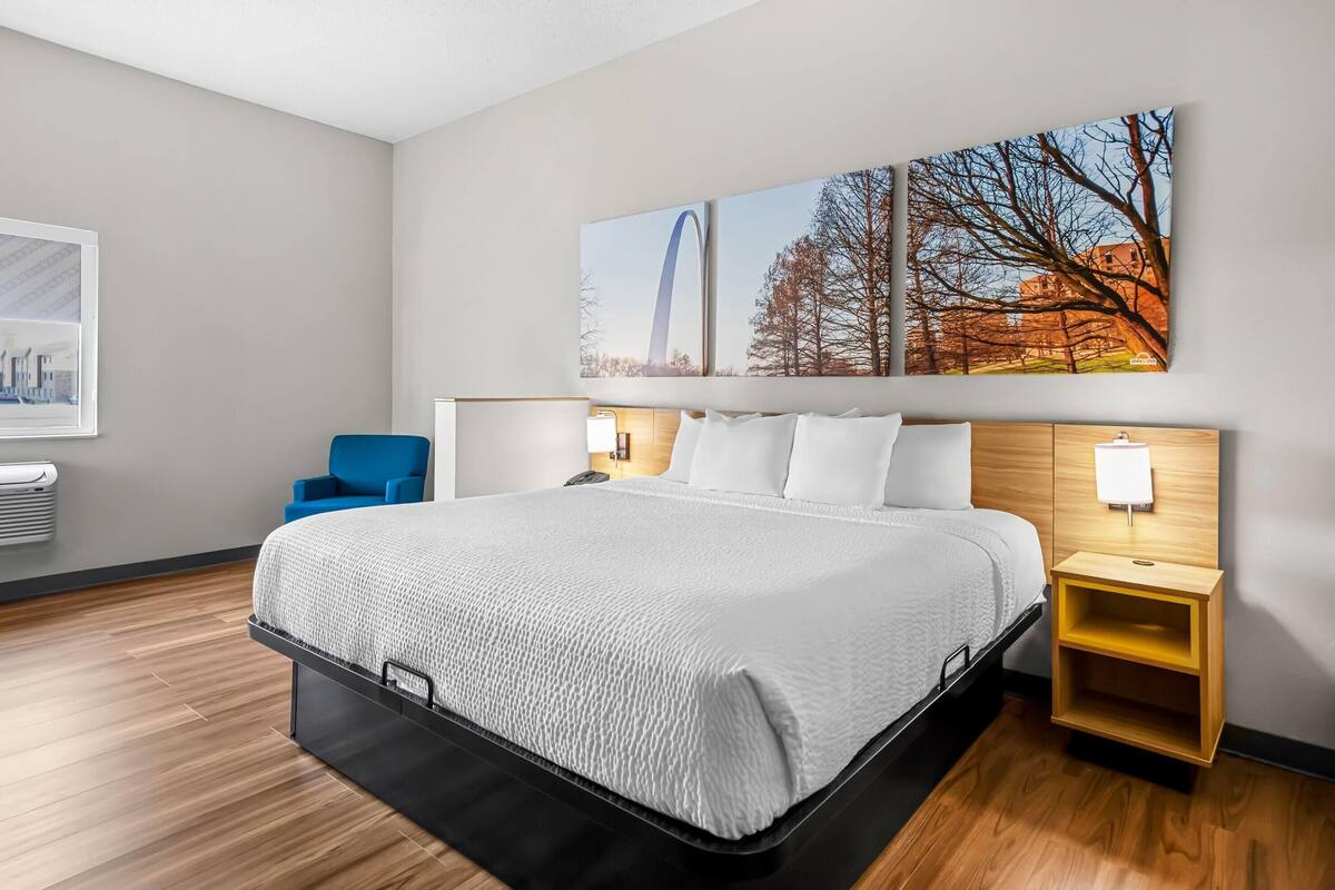 A modern hotel room with a large bed, a blue chair, and a wall-mounted TV.