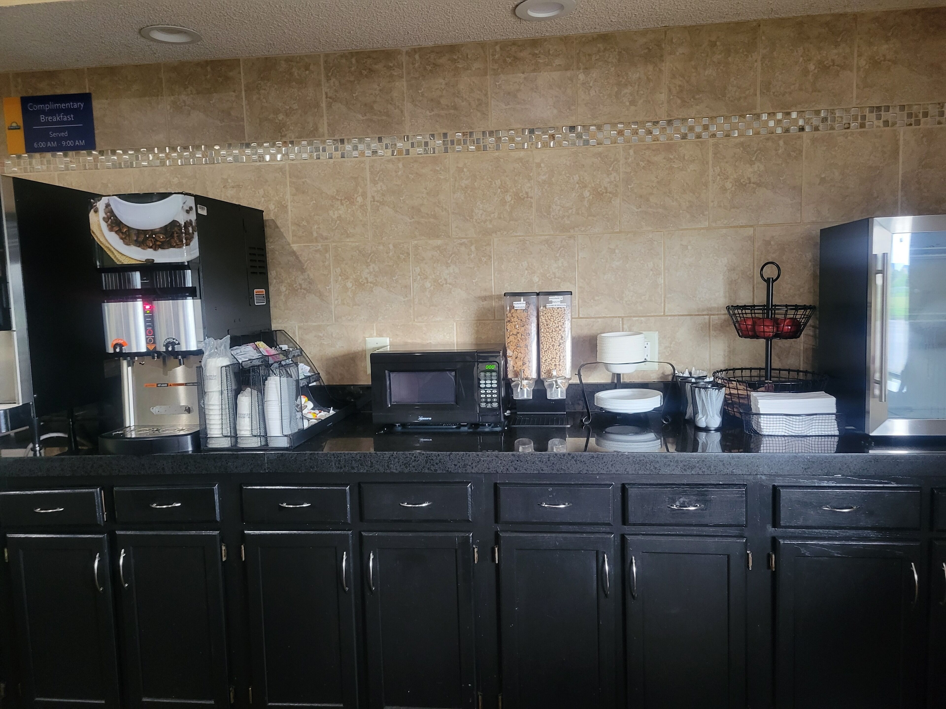 Cocina de hotel con cafetera, microondas y letrero de desayuno gratuito.