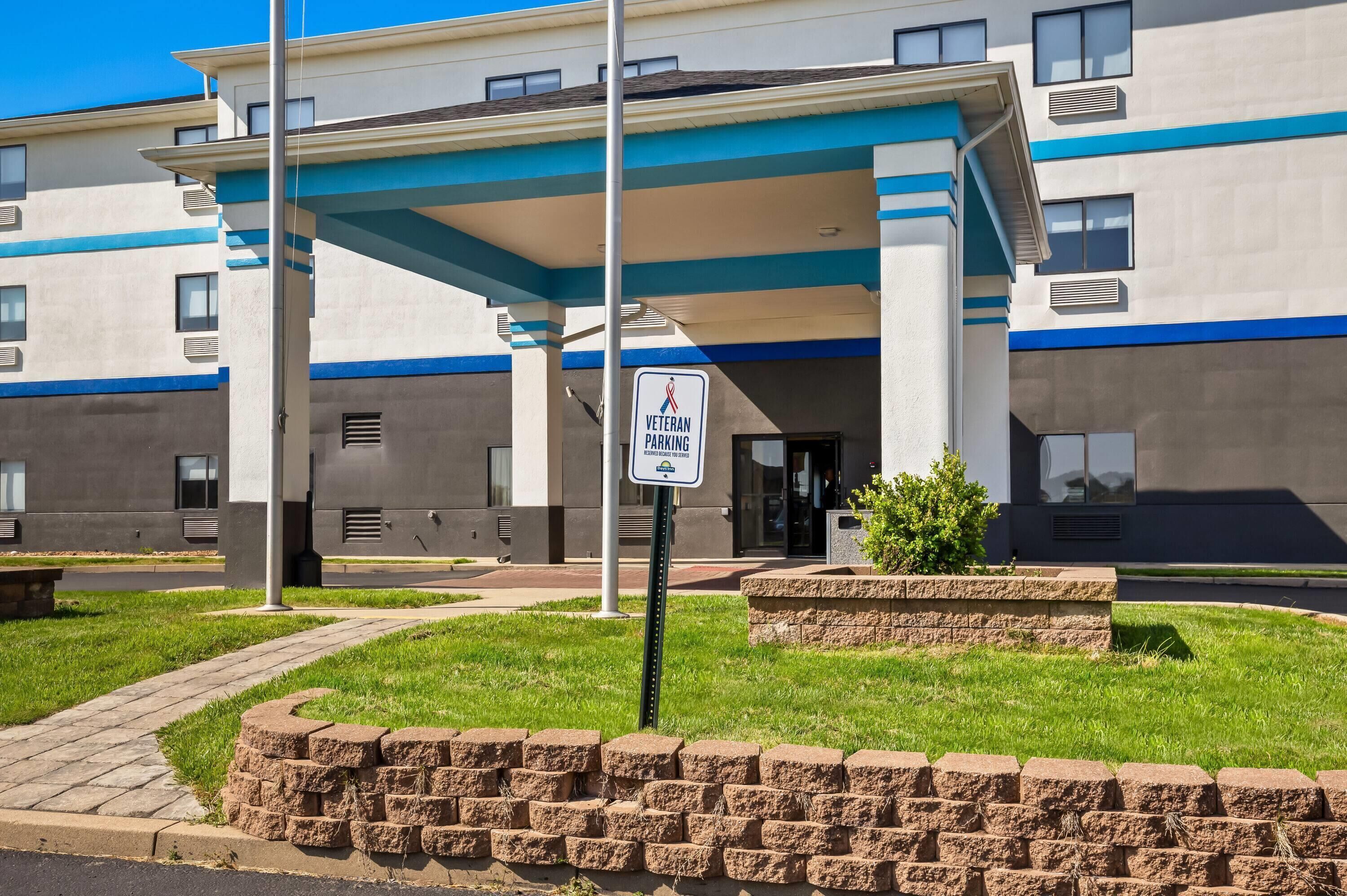 A modern building with a 'Veteran Parking' sign, a covered entrance, and a landscaped area with a stone wall.